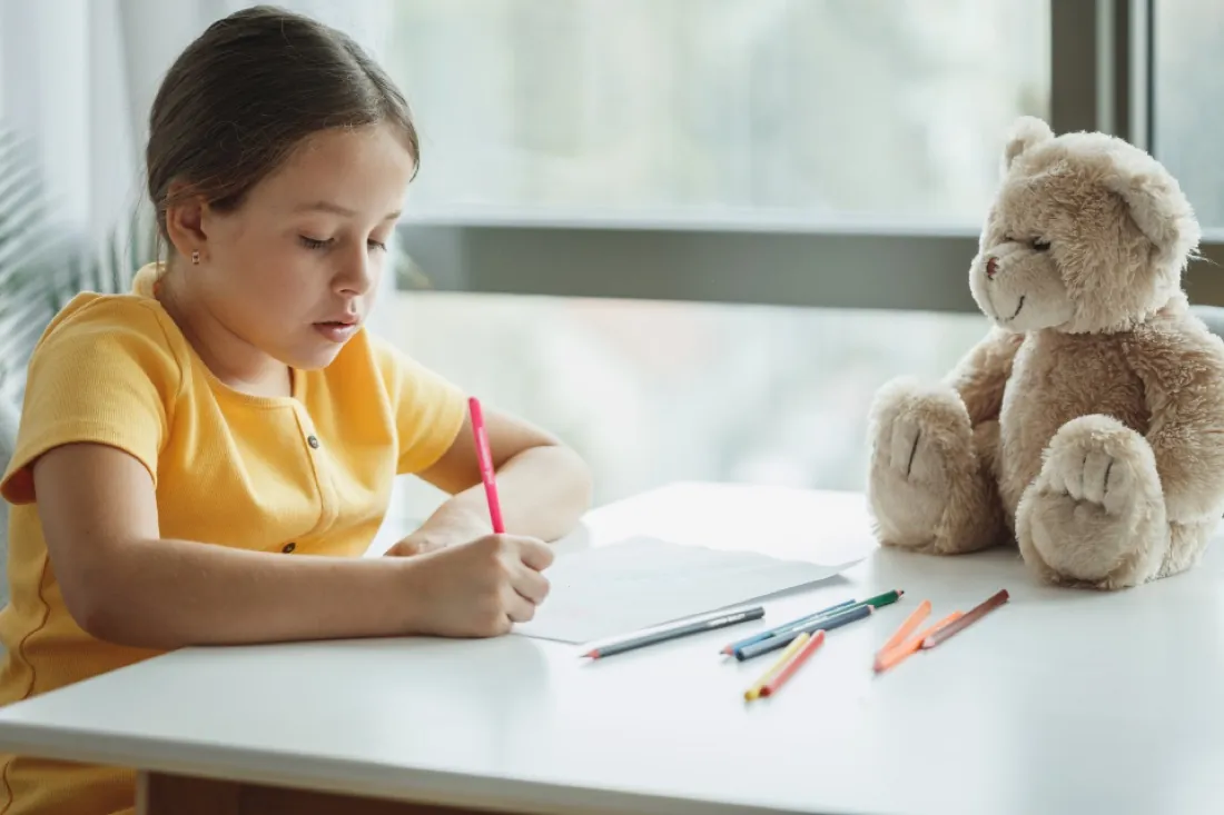 A young girl concentrating on writing at a bright desk